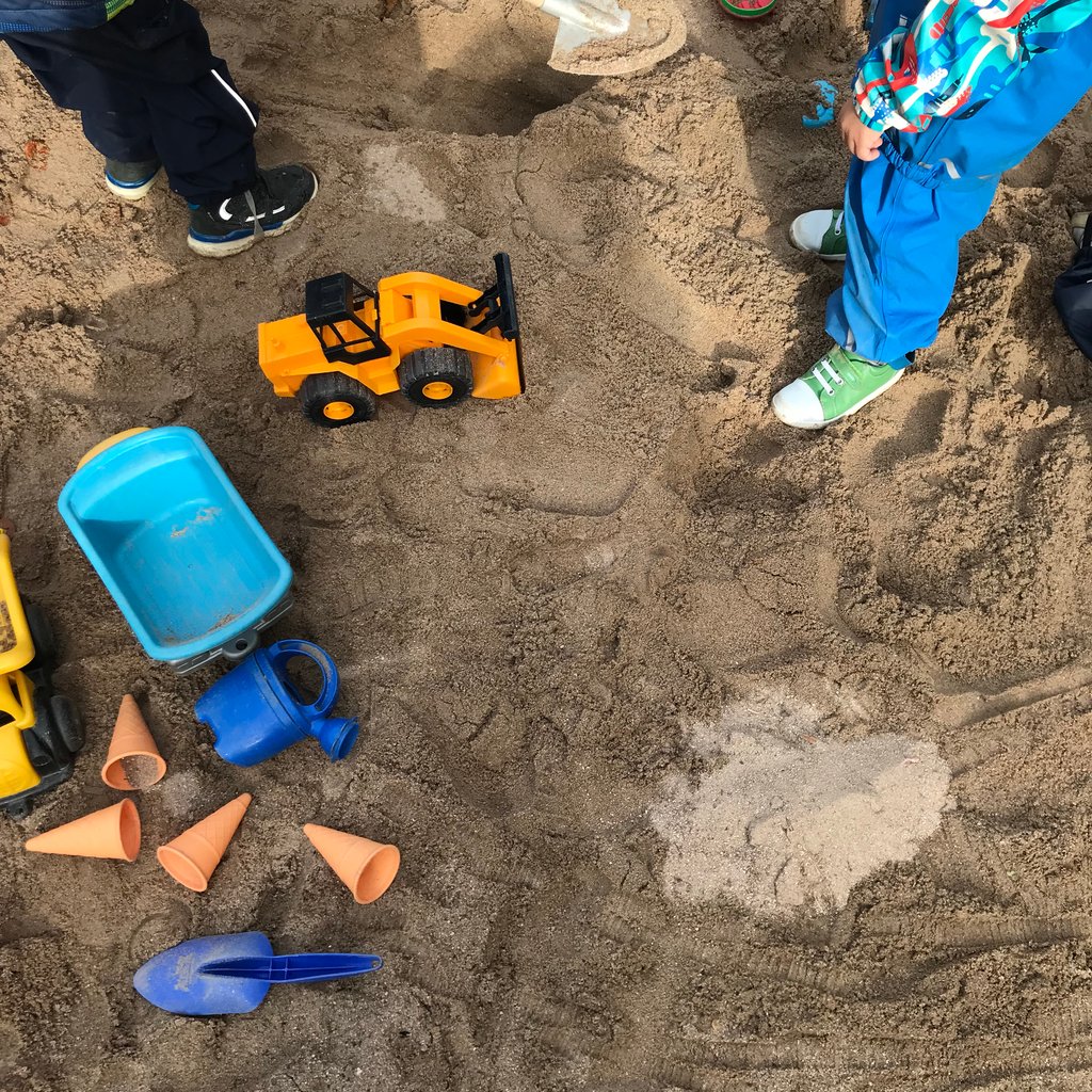 Kind spielt mit einem Spielzeugbagger im Sandkasten