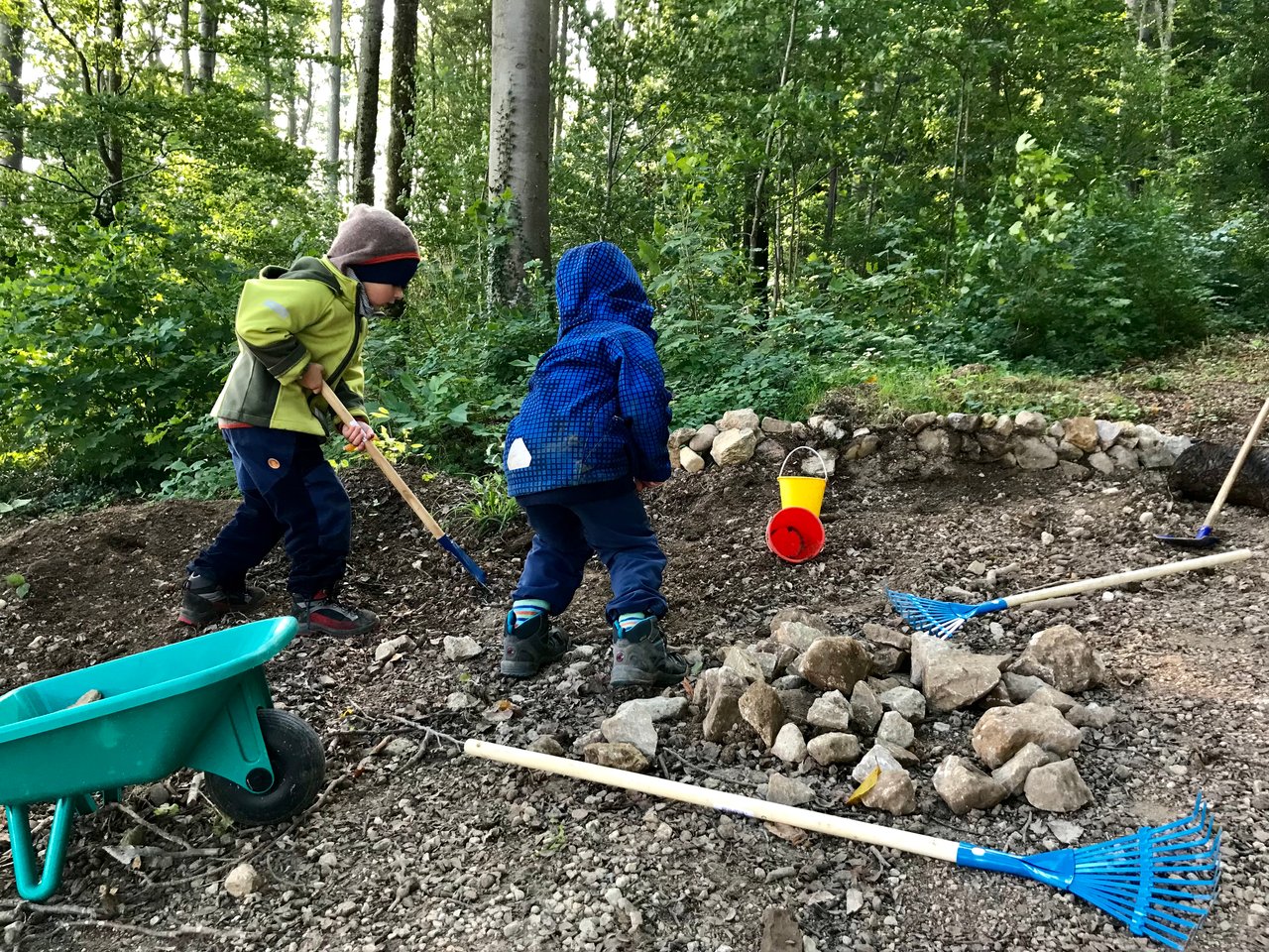 Zwei Kinder graben mit Gartenwerkzeug auf einer Waldlichtung