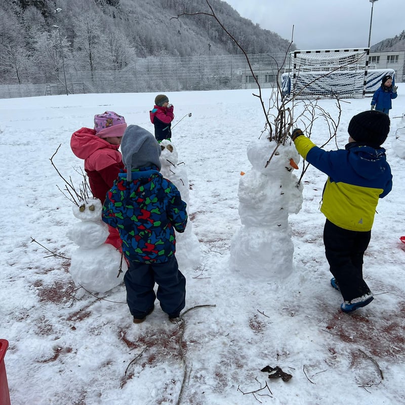 Kinder bauen gemeinsam Schneemänner auf der verschneiten Wiese
