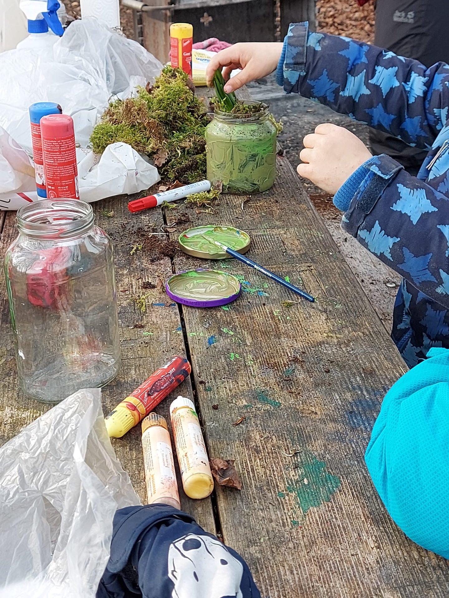 Kind bastelt mit Sand, Moos und Farben am Tisch