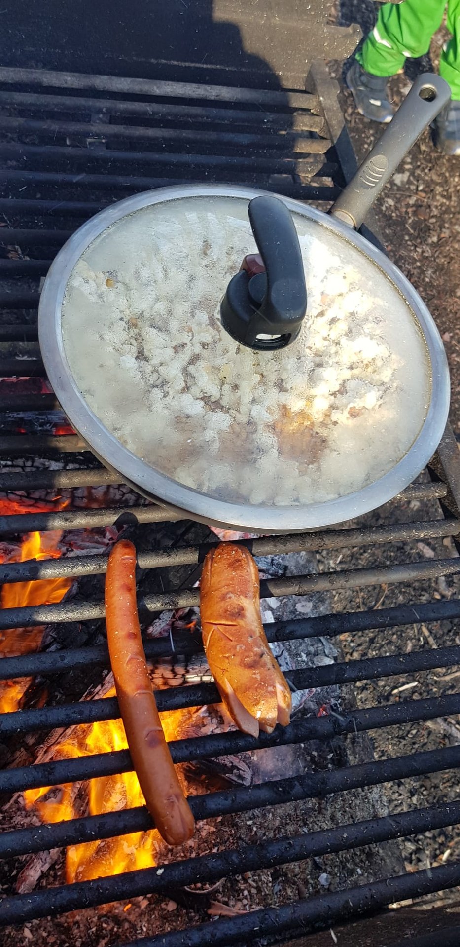 Bratwürste und Kartoffeln brutzeln auf dem Grill über dem Feuer