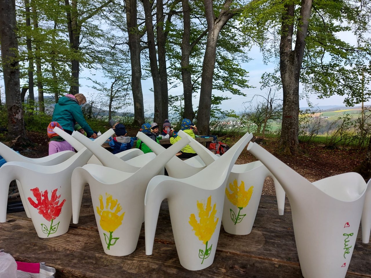 Bemalte Giesskannen mit Tulpenmotiven stehen auf einem Tisch im Wald